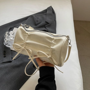 Close-up of cream PU leather cylinder bag featuring elegant bow knots and pleat details
