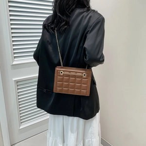 Sac à bandoulière marron matelassé avec chaîne dorée porté sur un blazer noir et jupe blanche