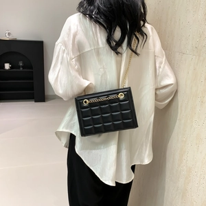 Sac sous l'aisselle matelassé noir avec chaîne dorée porté par un mannequin en blanc