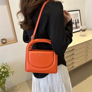 Chic orange leather mini square bag with circular handle worn by a model in a cozy setting