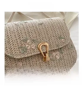 Close-up of beige woven straw bag featuring floral embroidery and gold metal clasp