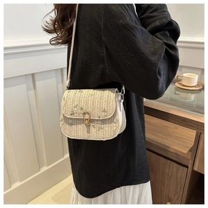 Detail of beige woven crossbody bag featuring floral embroidery and gold horseshoe clasp