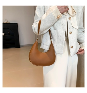 Brown half-moon shoulder bag in matte leather finish shown on model in a modern interior