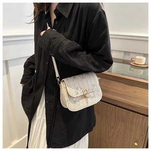 Detail of floral embroidery and gold horseshoe buckle on woven white crossbody bag
