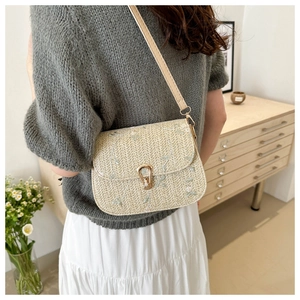 Close-up of floral embroidery on beige straw saddle bag with gold metal buckle