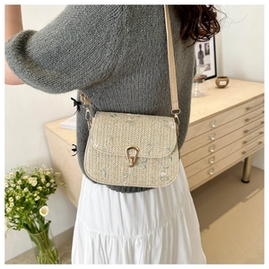 Detail of floral embroidery and gold horseshoe clasp on the woven crossbody bag
