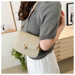 Detail of floral embroidery and gold horseshoe buckle on woven straw crossbody bag