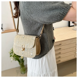 Close-up of beige straw shoulder bag featuring floral embroidery and gold horseshoe buckle