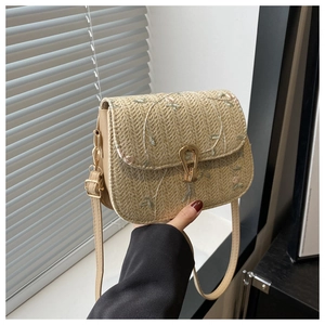 Detail of beige straw crossbody bag featuring floral embroidery and gold U-shaped metal buckle
