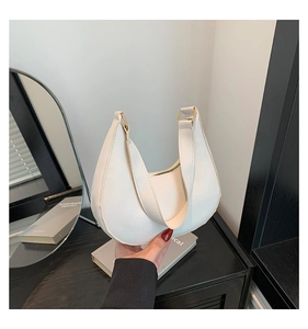 Detail of white leather crescent shoulder bag with golden hardware and textured finish
