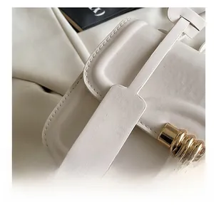 Close-up of white textured leather shoulder bag with golden metal ring and logo tag