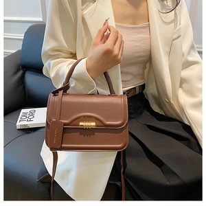 Detailansicht der braunen Lederhandtasche mit Goldverschluss, gehalten von einem Modell