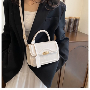 Detail shot of a cream leather square crossbody bag with gold hardware and logo tag