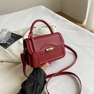 Detailaufnahme einer dunkelroten kleinen Tasche mit Goldschloss und modischem Anhänger