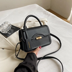 Details der schwarzen Lederhandtasche mit goldenem Zylinderschloss und modischem Anhänger