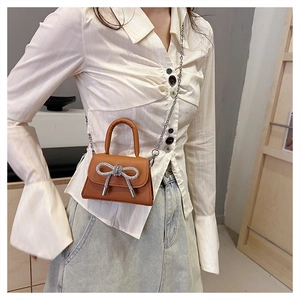 Detail of tan leather crossbody bag with a large silver rhinestone bow and chain strap