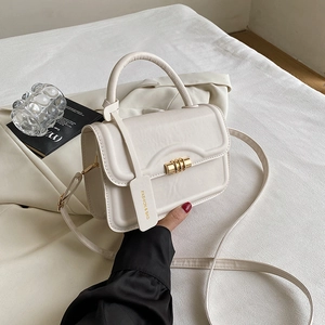 Detail einer beigen Lederhandtasche mit goldenem Zylinderdrehschloss und Ziernähten