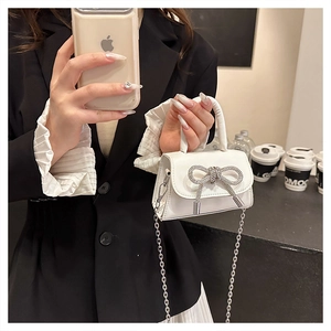 Close-up of white mini handbag featuring a crystal bow detail and silver chain strap