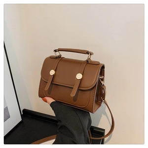 Close-up of brown retro faux leather flap bag with dual metallic buckles and top handle