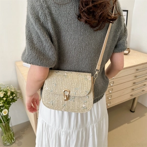Straw crossbody bag with floral embroidery and gold twist lock shown on a model