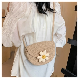 Dettaglio di borsa a sella intrecciata beige con motivo margherita indossata da modella