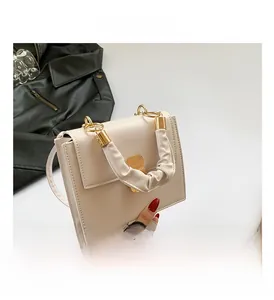 Close-up of beige leather square handbag with golden buckle and pleated handle detail
