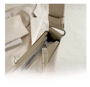 Detailed macro view of the smooth metal zipper and textured beige leather on saddle bag