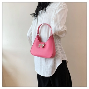 Pink crescent shoulder bag with silver bow detail worn by a model in casual style