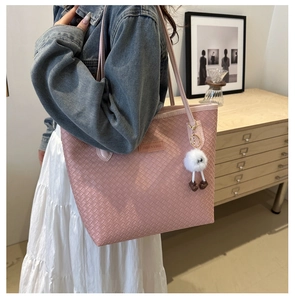 Sac fourre-tout tissé rose avec porte-clé en peluche blanche dans un décor intérieur