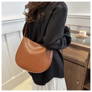 Minimalist brown lychee leather half-moon shoulder bag worn in an elegant lifestyle setting