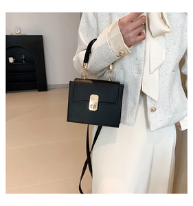 Detail of black matte leather handbag featuring gold ring handle and metal clasp closure