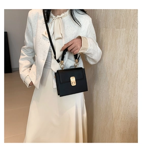 Detail of mini black square bag with gold lock and unique ruffled leather ring handle