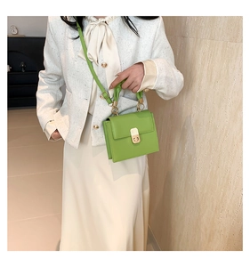 Detail of green structured handbag featuring a pleated top handle and gold clasp