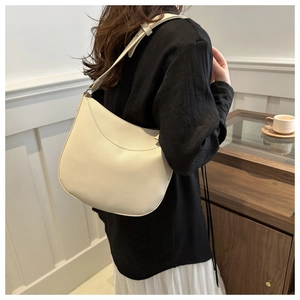 Detail of a creamy white textured leather hobo bag worn by a model in a minimal setting