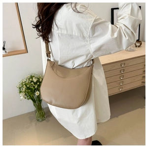 Litchi texture crescent saddle bag in khaki leather worn by a model in a minimal room