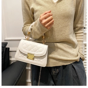 Detail of white quilted crossbody bag featuring golden lock and elegant chain strap