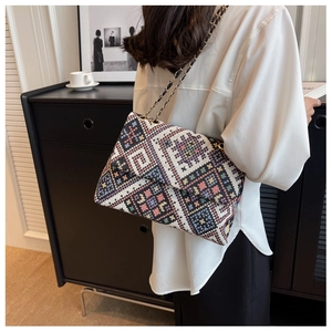 Detail of geometric ethnic embroidery on a chain shoulder bag worn by a model