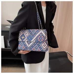 Detail of a geometric ethnic embroidery tote bag with a gold metal and leather chain strap