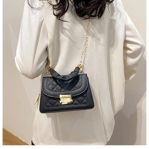 Detail of black quilted leather shoulder bag with gold chain and pleated handle worn by model