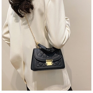 Detail of black quilted shoulder bag with gold chain strap worn over a white blazer