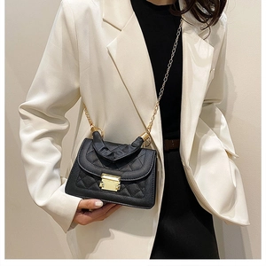 Detail of a black quilted crossbody bag with gold chain strap on a white suit model
