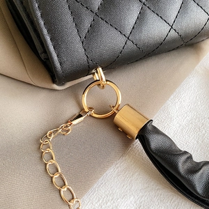 Detailed close-up of black quilted leather texture with gold metal chain and tassel