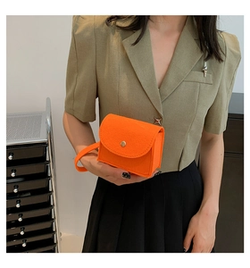 Detail of orange felt handbag with gold snap button held by a model in green blazer