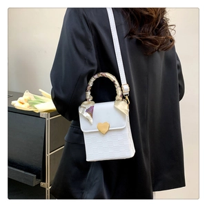 Detailed view of white woven crossbody bag with heart buckle and scarf-wrapped handle