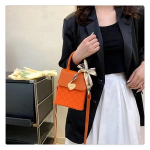 Detail of orange crossbody bag with heart lock, woven texture and decorative silk scarf