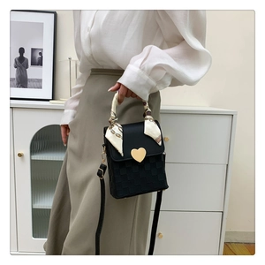 Close-up of black crossbody bag with woven texture, gold heart buckle, and silk scarf handle