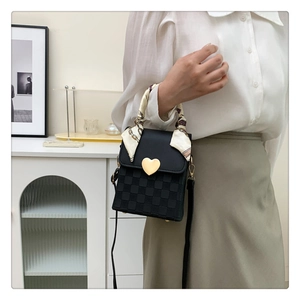 Detail of black crossbody bag with checkered flap, gold heart buckle and silk scarf handle