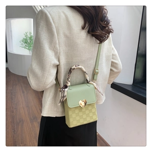 Detail of light green crossbody bag with gold heart buckle and checkered texture