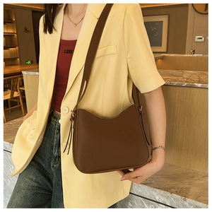 Détail d'un sac à bandoulière minimaliste en cuir marron avec design incurvé et sangle large