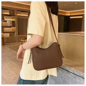 Détail du sac hobo en cuir marron foncé avec cordon à pompon porté par un mannequin